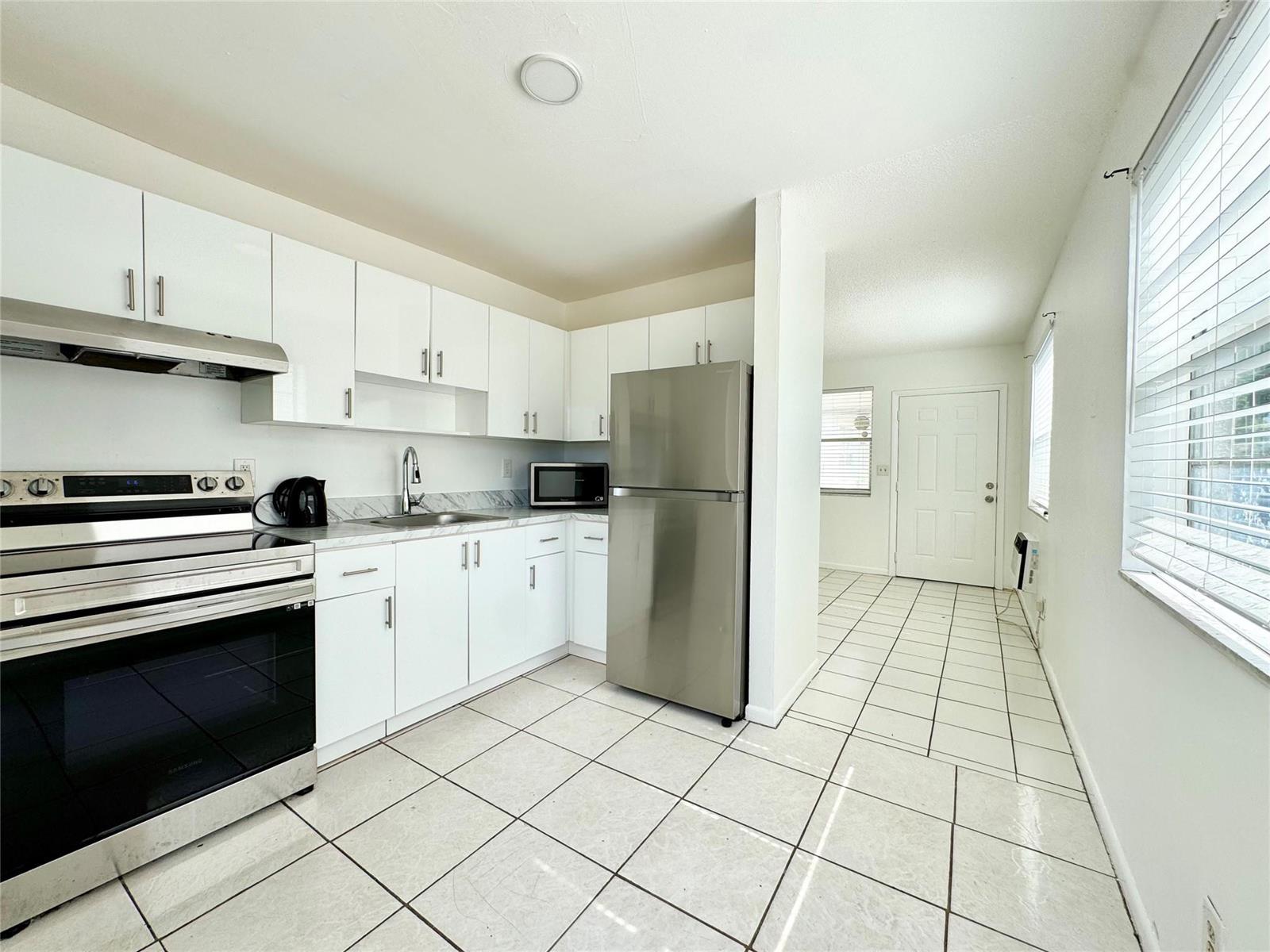 A kitchen features white cabinets, stainless steel appliances, and light-colored tile flooring — 147 W 17th Street, Riviera Beach FL 33404, RIVIERA BEACH, FL