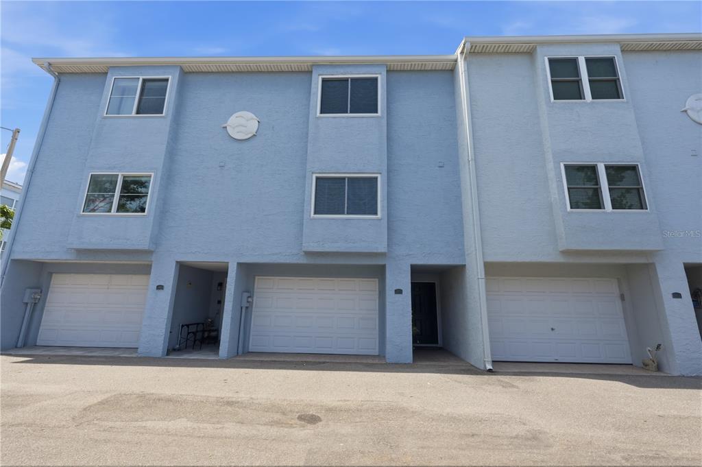 The exterior of a three-story blue townhouse features three garage doors and multiple windows — 545 PINELLAS BAYWAY S UNIT 302, ST PETERSBURG, FL