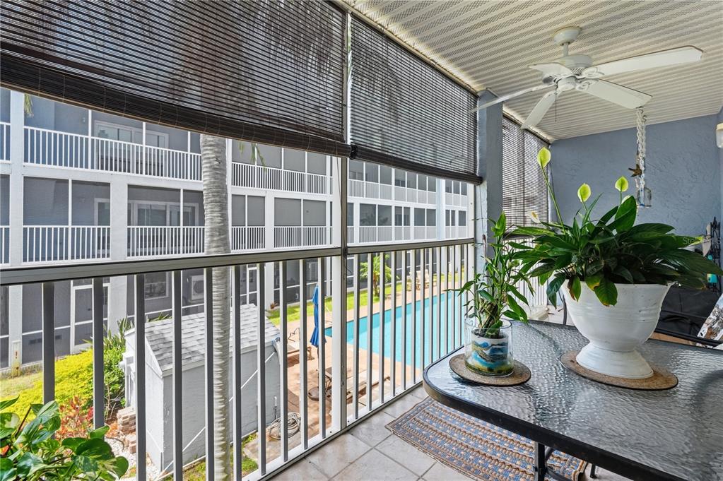 A screened-in balcony overlooks a swimming pool and features a ceiling fan and potted plants — 545 PINELLAS BAYWAY S UNIT 302, ST PETERSBURG, FL