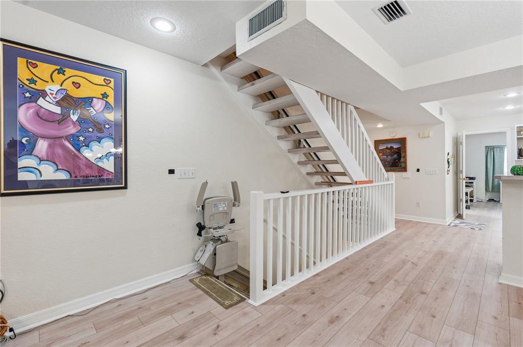 A staircase with a chair lift and white railing sits in a room with wood flooring — 545 PINELLAS BAYWAY S UNIT 302, ST PETERSBURG, FL
