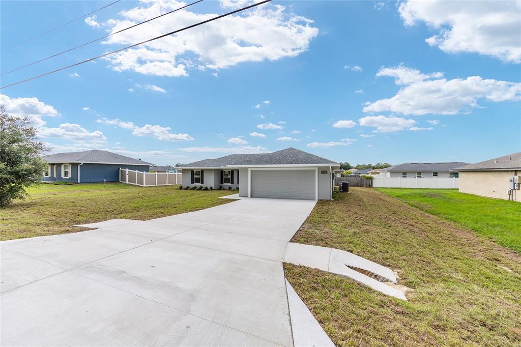 A single-story house with a gray garage and a concrete driveway under a blue sky — 12371 SE 100TH AVENUE, BELLEVIEW, FL