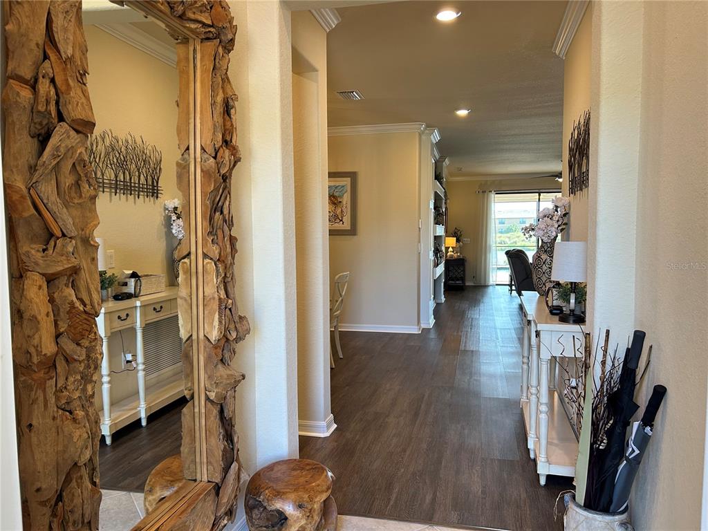 A hallway with wood-look flooring leads to a living area with a view of water — 6808 WILD LAKE TERRACE, BRADENTON, FL