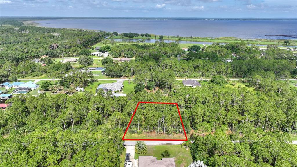 An aerial view shows a wooded, rectangular lot outlined in red near a large lake — 25 AMARYLLIS DRIVE, INDIAN LAKE ESTATES, FL