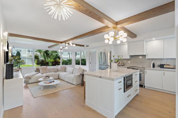 An open-concept kitchen and living area features wood ceiling beams, white cabinetry, and a sectional — 320 S Ocean Boulevard # c, Delray Beach FL 33483, DELRAY BEACH, FL