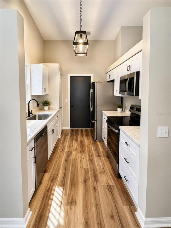 A galley kitchen features white cabinets, stainless steel appliances, and wood-look flooring — 3604 NW 51ST TERRACE, GAINESVILLE, FL