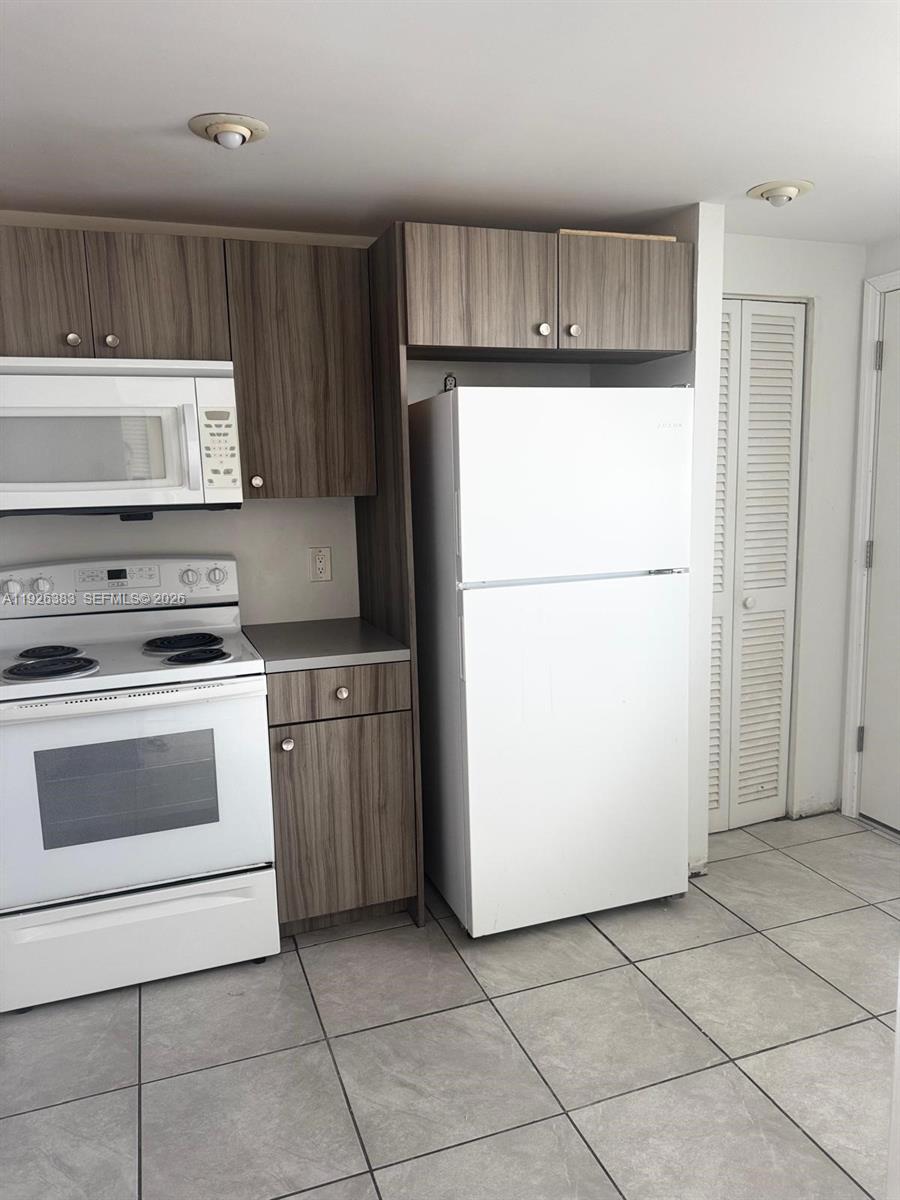 A kitchen features white appliances, wood-grain cabinets, and light-colored tile flooring — 1770 NE 191st St # 1, Miami FL 33179, MIAMI, FL