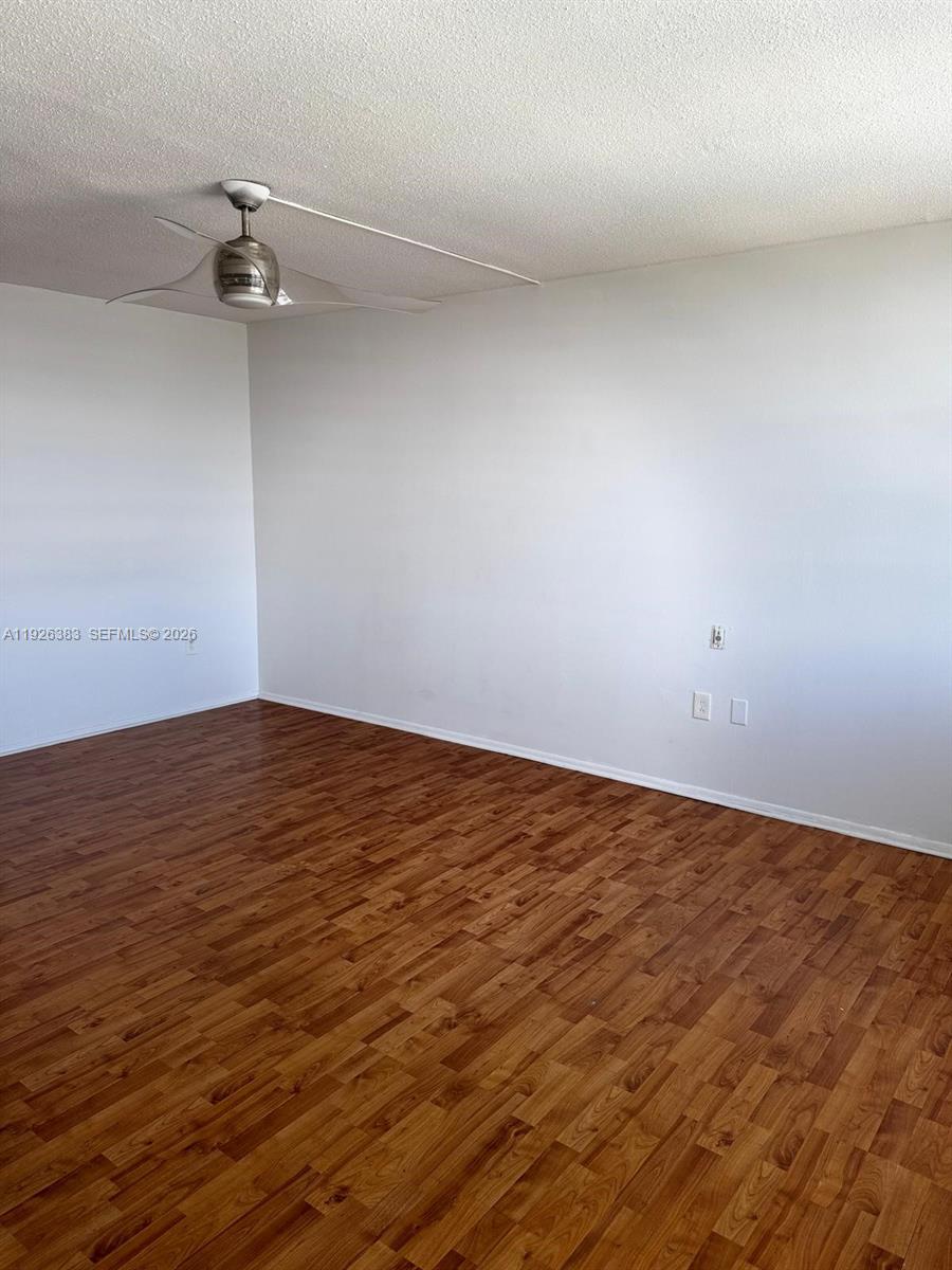 An empty room features wood-look laminate flooring, white walls, and a ceiling fan — 1770 NE 191st St # 1, Miami FL 33179, MIAMI, FL