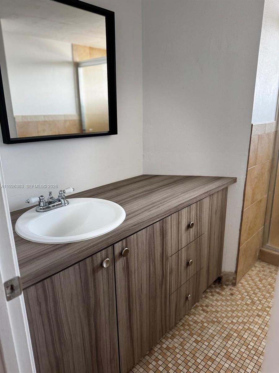 A bathroom vanity features a wood-grain cabinet, a white sink, and a black-framed mirror — 1770 NE 191st St # 1, Miami FL 33179, MIAMI, FL