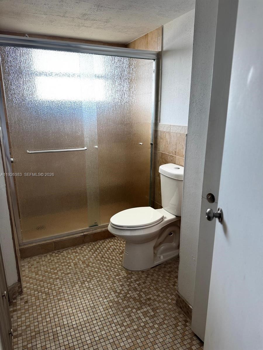 A bathroom features a tiled shower with sliding glass doors and a white toilet — 1770 NE 191st St # 1, Miami FL 33179, MIAMI, FL