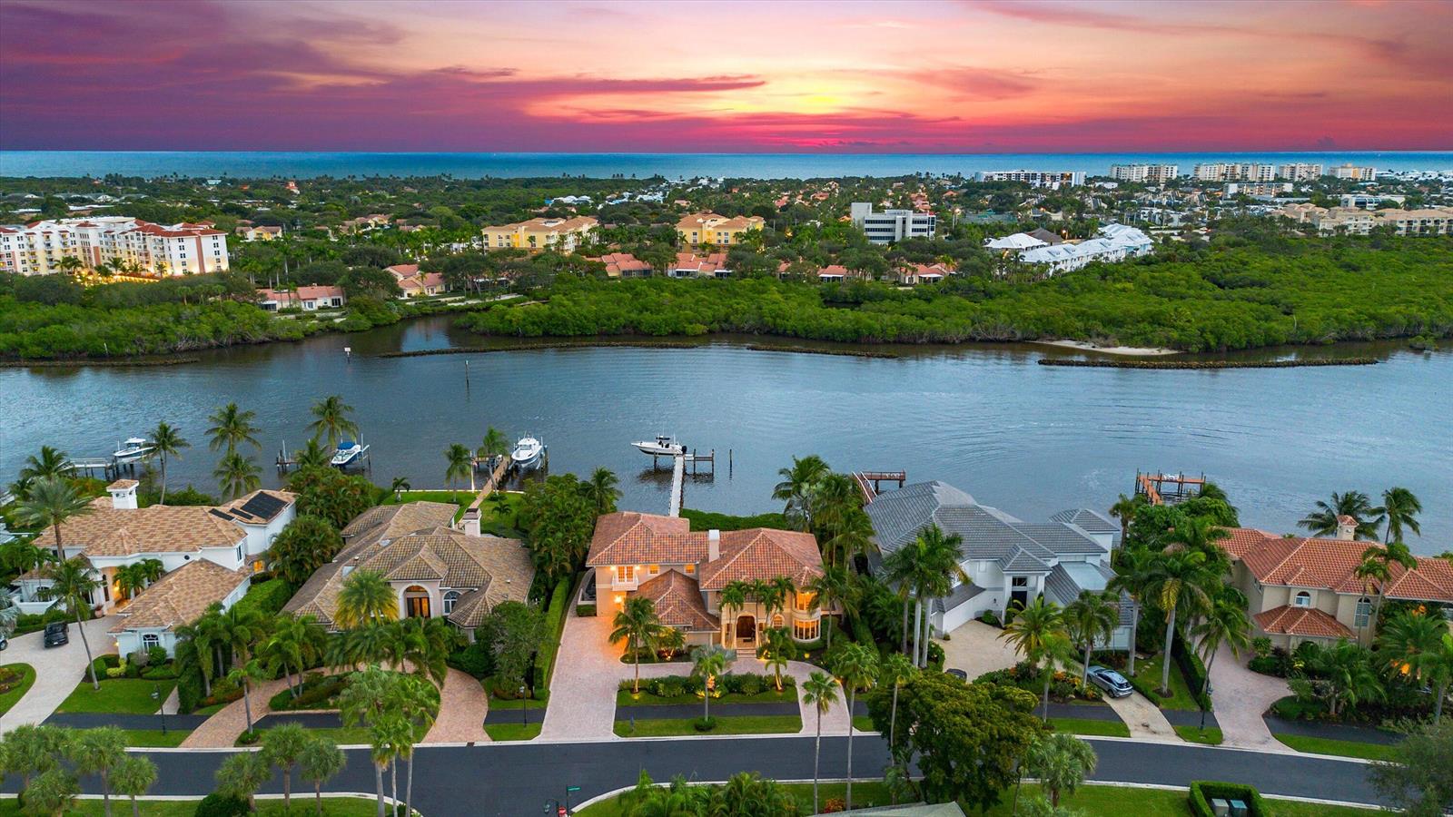 An aerial view shows waterfront homes with tiled roofs along a canal at sunset — 3164 Casseekey Island Road, Jupiter FL 33477, JUPITER, FL