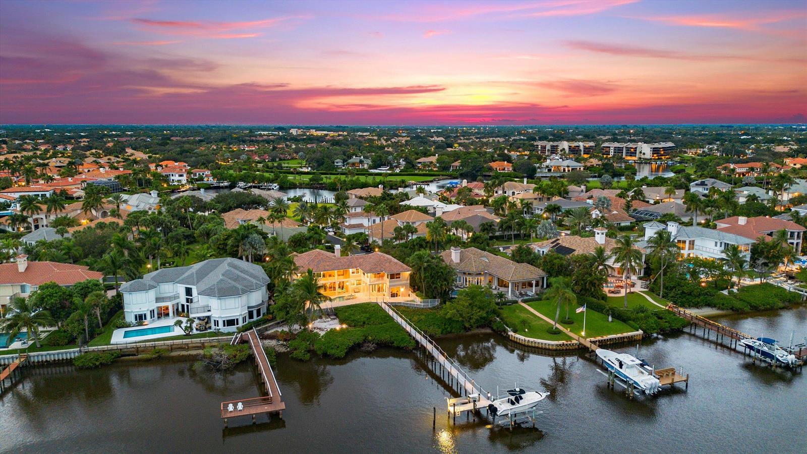 An aerial view shows several waterfront houses with private docks along a canal at sunset — 3164 Casseekey Island Road, Jupiter FL 33477, JUPITER, FL