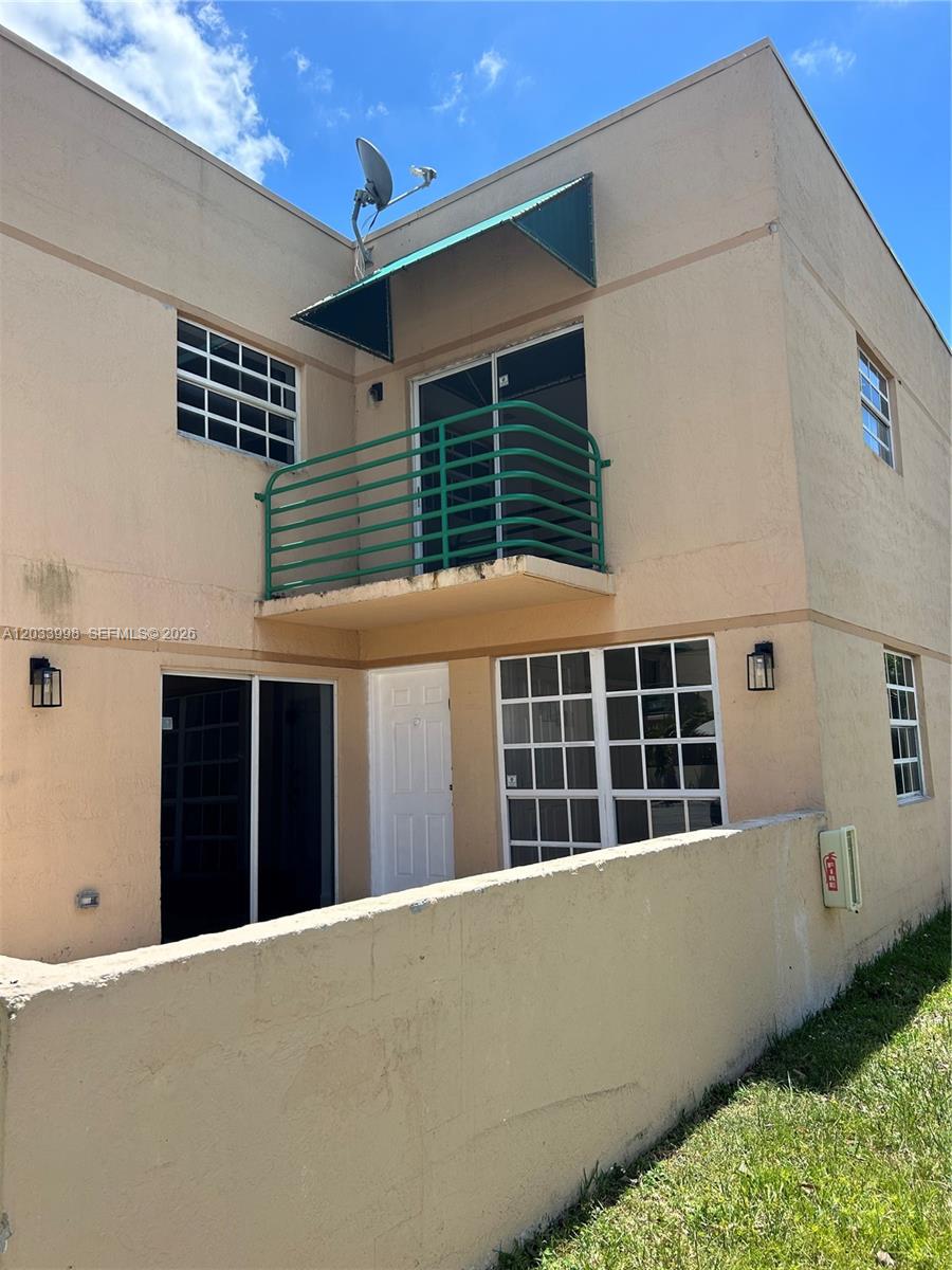 The exterior of a two-story stucco building features a green balcony and a small patio — 11880 SW 19th Ter # 113, Miami FL 33175, MIAMI, FL