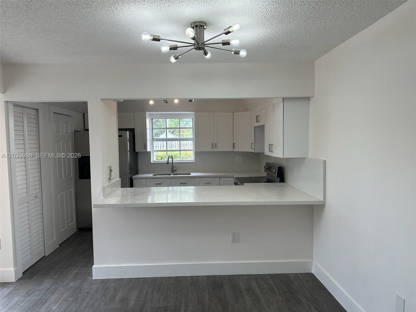 A kitchen with white cabinets and a quartz breakfast bar overlooks a living area — 11880 SW 19th Ter # 113, Miami FL 33175, MIAMI, FL