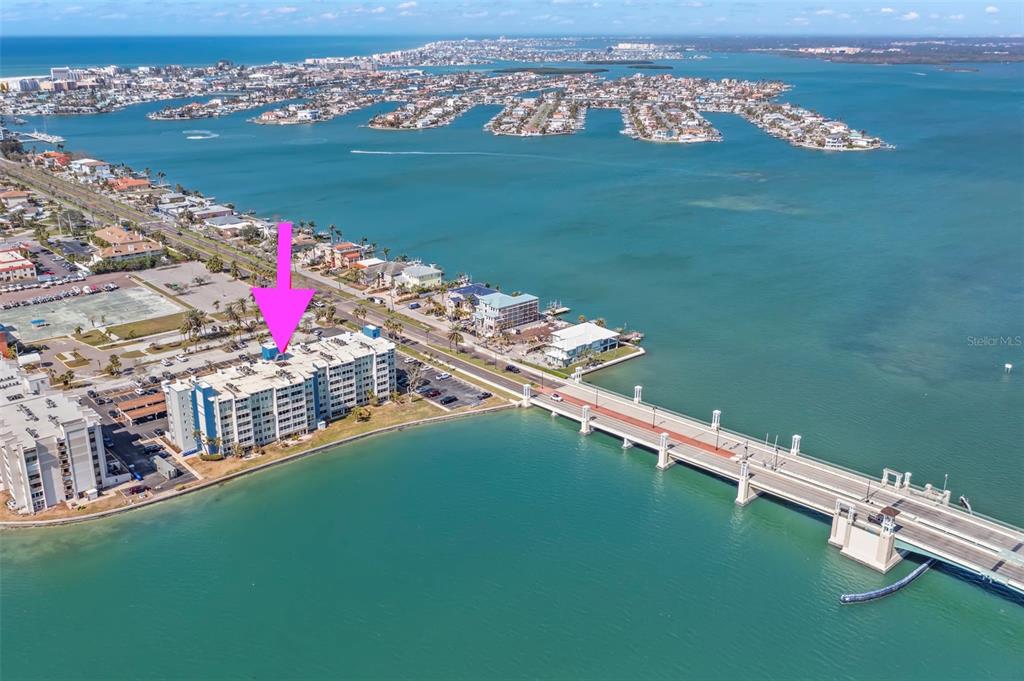 An aerial view shows a multi-story waterfront condominium building next to a bridge — 500 TREASURE ISLAND CAUSEWAY UNIT 205, TREASURE ISLAND, FL
