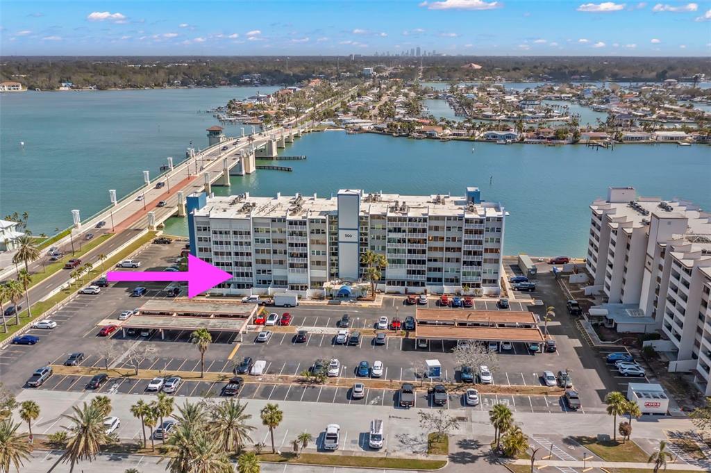 An aerial view shows a multi-story apartment building with a parking lot and a bridge — 500 TREASURE ISLAND CAUSEWAY UNIT 205, TREASURE ISLAND, FL