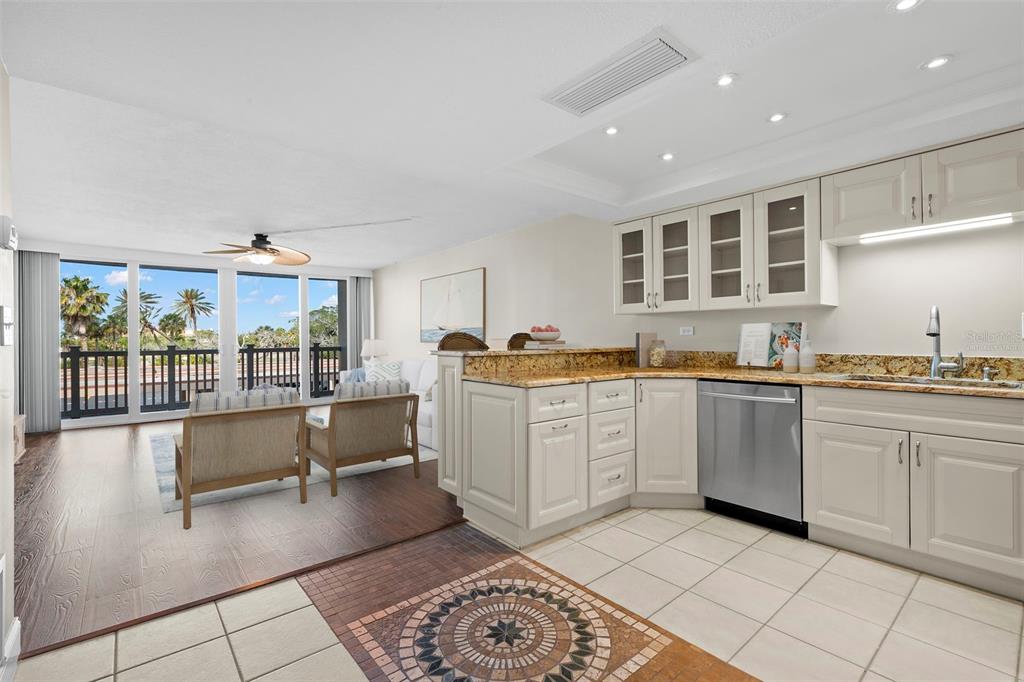 A kitchen with light cabinets and granite countertops overlooks a living area with balcony access — 500 TREASURE ISLAND CAUSEWAY UNIT 205, TREASURE ISLAND, FL
