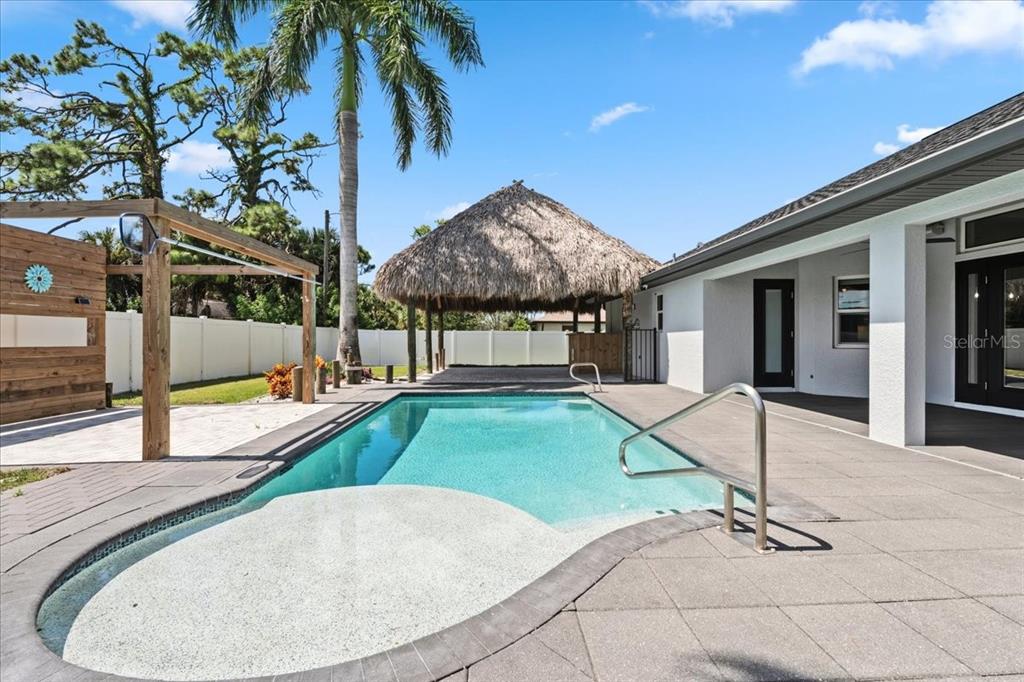 A swimming pool with a tanning ledge sits on a patio next to a tiki hut — 2415 W PRICE BOULEVARD, NORTH PORT, FL