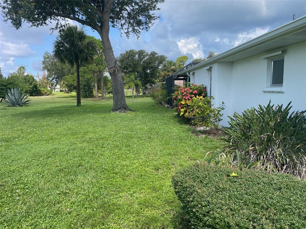 A side view of a white house exterior with a lawn, trees, and landscaping — 1091 VENTURE COURT, PUNTA GORDA, FL