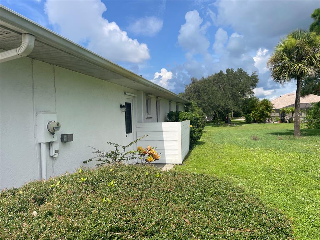 The exterior of a white building features a side door, a privacy screen, and landscaping — 1091 VENTURE COURT, PUNTA GORDA, FL