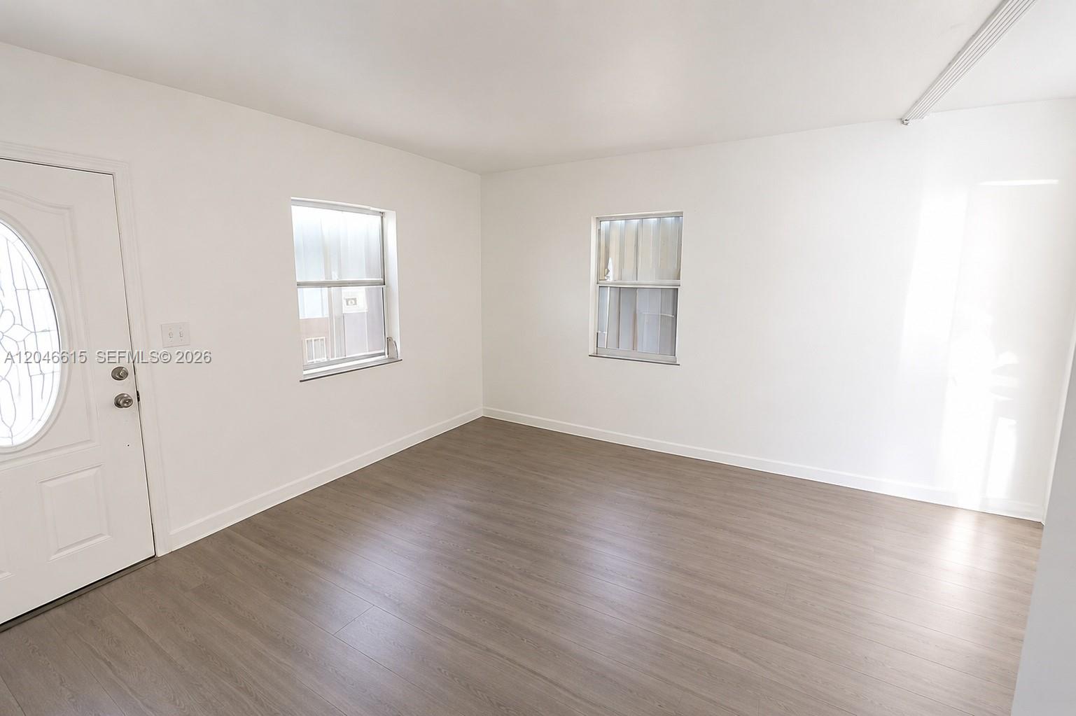 An empty room features white walls, light wood-look flooring, two windows, and a white door — 1211 Kasim St, Opa-Locka FL 33054, OPA-LOCKA, FL