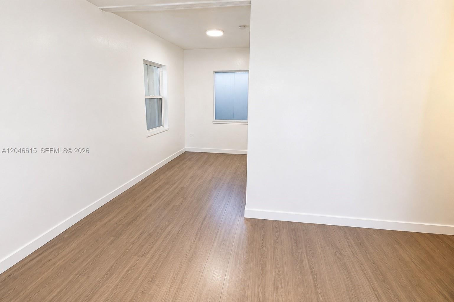 An empty room features white walls, wood-look flooring, and two windows — 1211 Kasim St, Opa-Locka FL 33054, OPA-LOCKA, FL