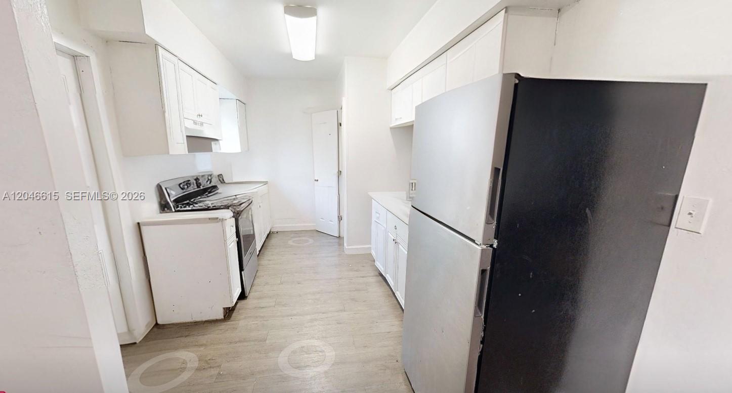 A narrow kitchen features white cabinets, stainless steel appliances, and light wood-look flooring — 1211 Kasim St, Opa-Locka FL 33054, OPA-LOCKA, FL