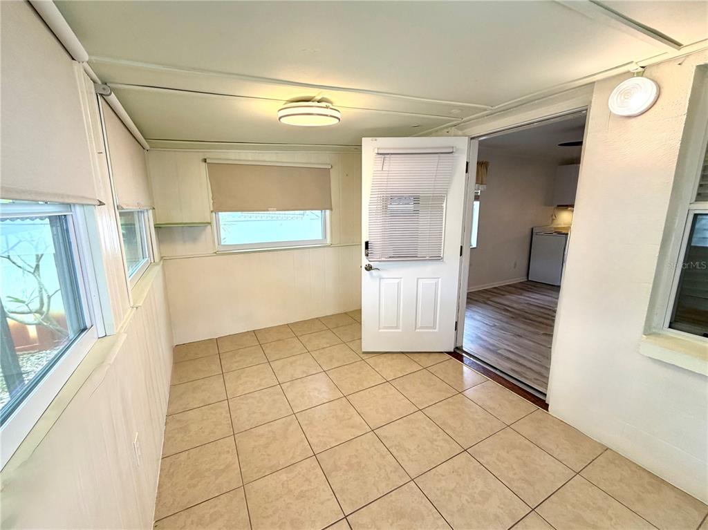 A sunroom with beige tile flooring, white walls, and a door leading into a kitchen — 516 NORTHMOOR AVENUE N, ST PETERSBURG, FL