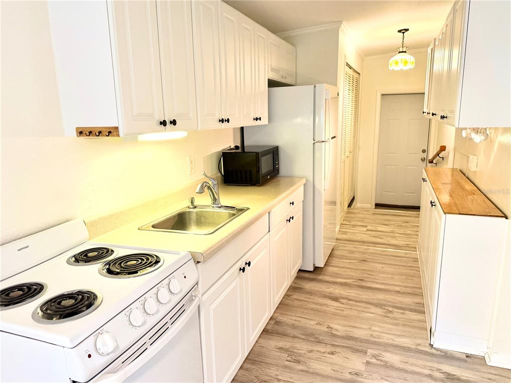 A white kitchen features a stove, sink, refrigerator, and light wood-look flooring — 516 NORTHMOOR AVENUE N, ST PETERSBURG, FL