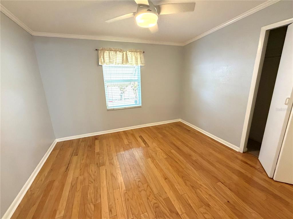 An empty bedroom features light blue walls, hardwood flooring, a ceiling fan, and a window — 516 NORTHMOOR AVENUE N, ST PETERSBURG, FL