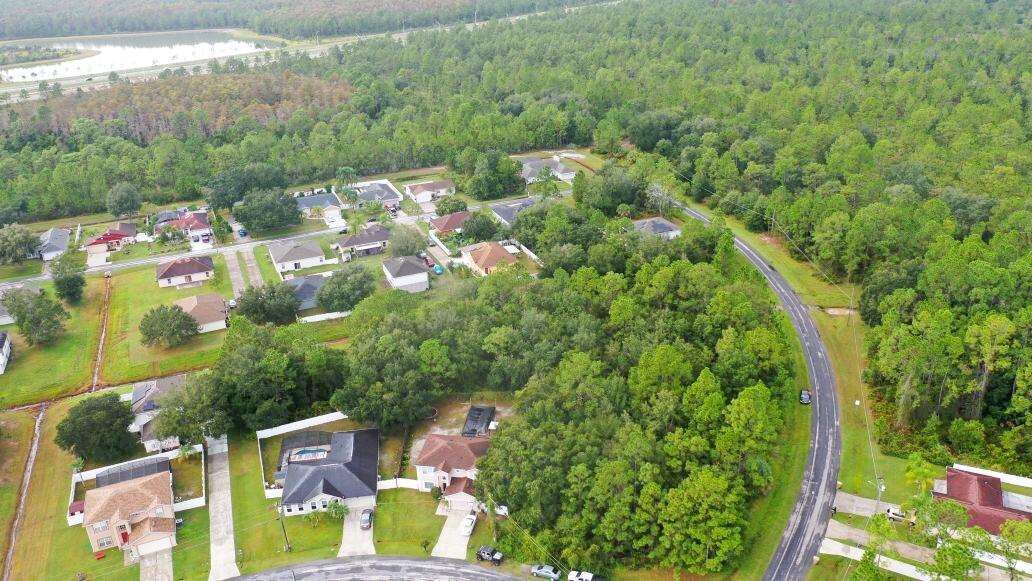 An aerial view shows a suburban neighborhood with houses surrounded by dense green forest — 0 Banbridge Drive, FL 34758, FL