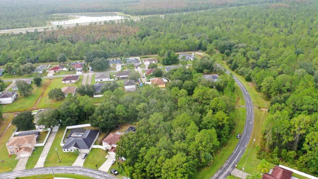 An aerial view shows a suburban neighborhood surrounded by dense forest and a nearby road — 0 Banbridge Drive, FL 34758, FL