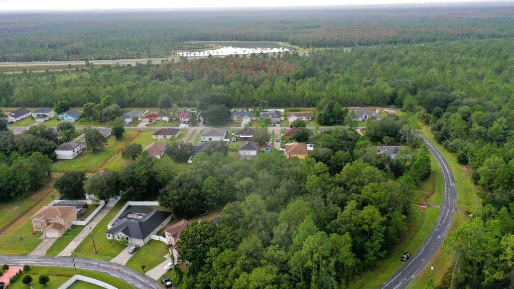 An aerial view shows a suburban neighborhood surrounded by dense forest and a nearby highway — 0 Banbridge Drive, FL 34758, FL