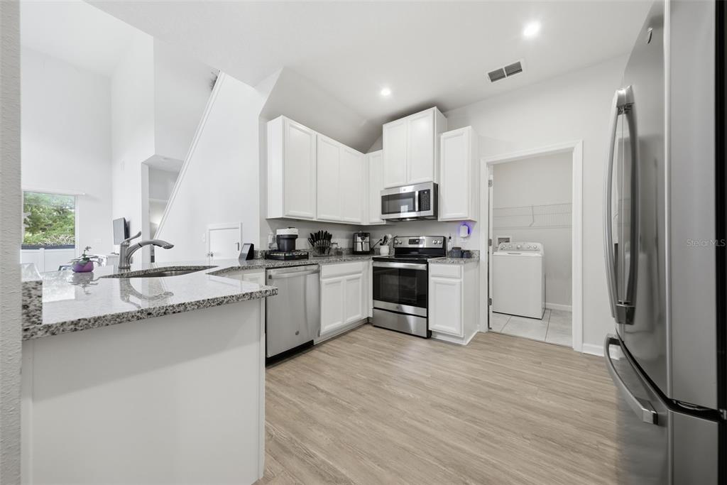 A modern kitchen features white cabinets, stainless steel appliances, granite countertops, and light wood flooring — 2130 LACEFLOWER DRIVE, BRANDON, FL