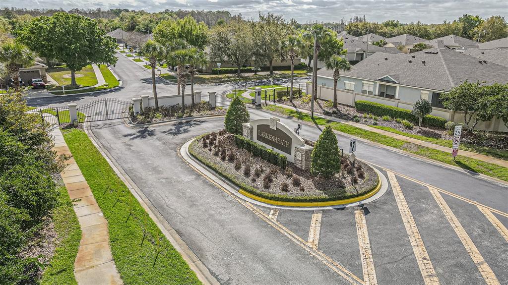 An aerial view shows the gated entrance to a residential community with a stone sign — 1123 BENSBROOKE DRIVE, WESLEY CHAPEL, FL