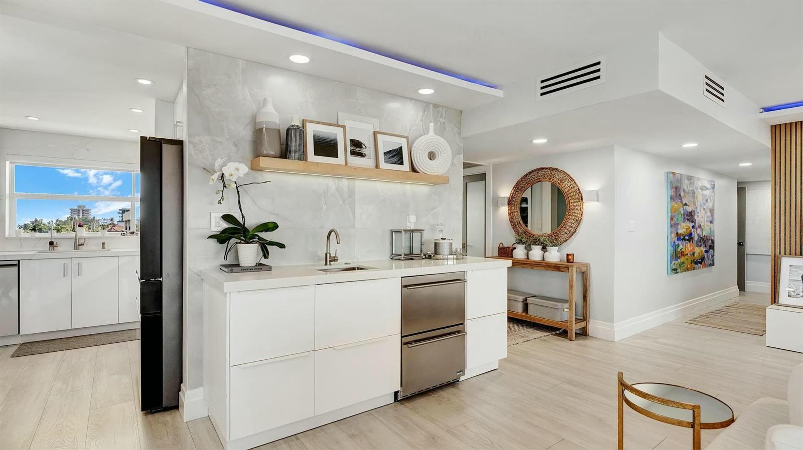 A modern kitchen and bar area featuring white cabinetry, marble-look walls, and stainless steel appliances — 2871 N Ocean Boulevard N # D502, Boca Raton FL 33431, BOCA RATON, FL