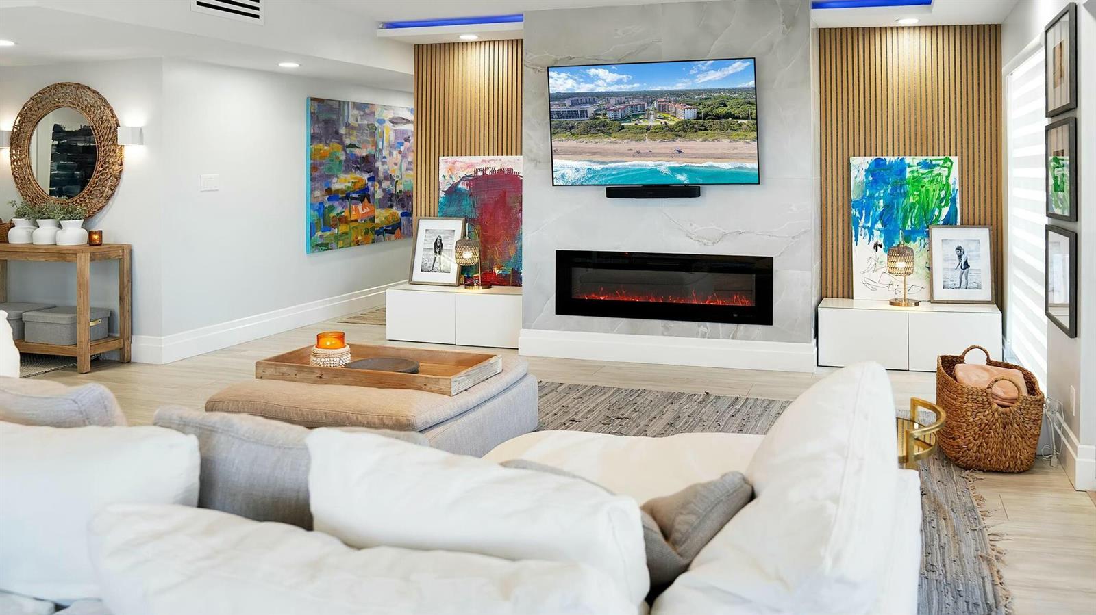 A living room features a marble fireplace, wall-mounted television, wood slat accents, and colorful artwork — 2871 N Ocean Boulevard N # D502, Boca Raton FL 33431, BOCA RATON, FL