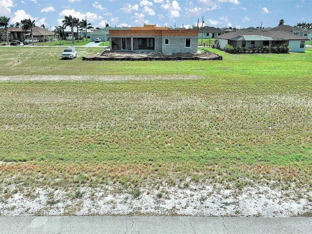 An unfinished concrete house stands on a large, grassy lot under a cloudy sky — 1037 NW 37TH PLACE, CAPE CORAL, FL