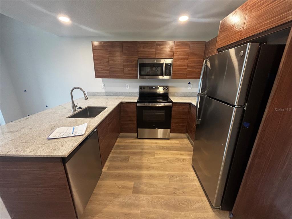 A kitchen features wood-grain cabinets, stainless steel appliances, and light-colored granite countertops — 4424 S TEXAS AVENUE UNIT 1-204, ORLANDO, FL