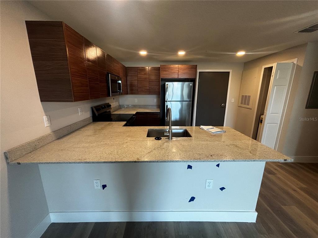 A kitchen features wood-grain cabinets, granite countertops, stainless steel appliances, and a breakfast bar — 4424 S TEXAS AVENUE UNIT 1-204, ORLANDO, FL