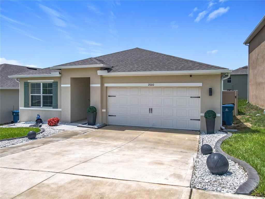 A single-story house with a beige stucco exterior, a two-car garage, and a concrete driveway — 2000 CHICKASAW BOULEVARD, DAVENPORT, FL