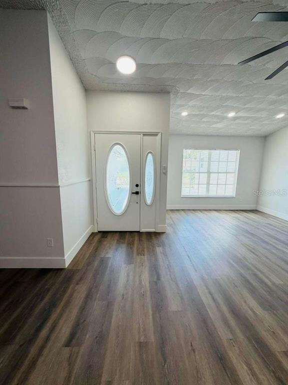 An entryway with wood-look flooring leads into a living area featuring a textured ceiling — 665 REGENCY WAY, KISSIMMEE, FL