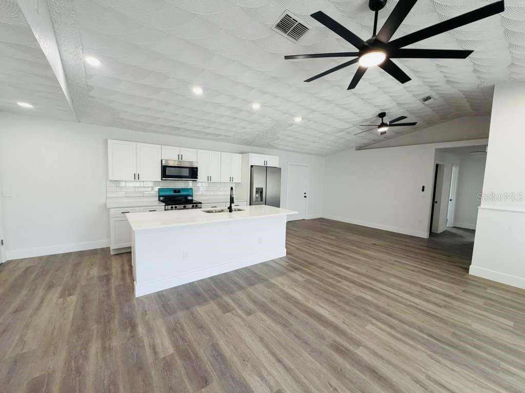 A modern kitchen with white cabinets, a central island, and wood-look flooring — 665 REGENCY WAY, KISSIMMEE, FL