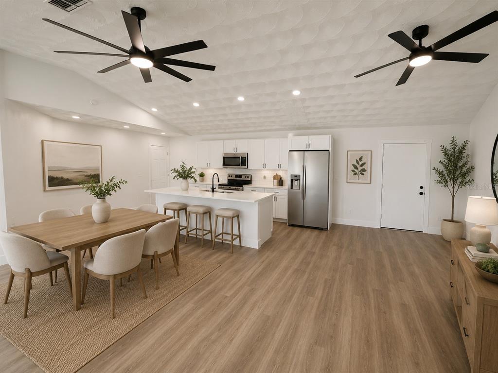 A bright open-concept kitchen and dining area features white cabinetry, a central island, and wood-look flooring — 665 REGENCY WAY, KISSIMMEE, FL