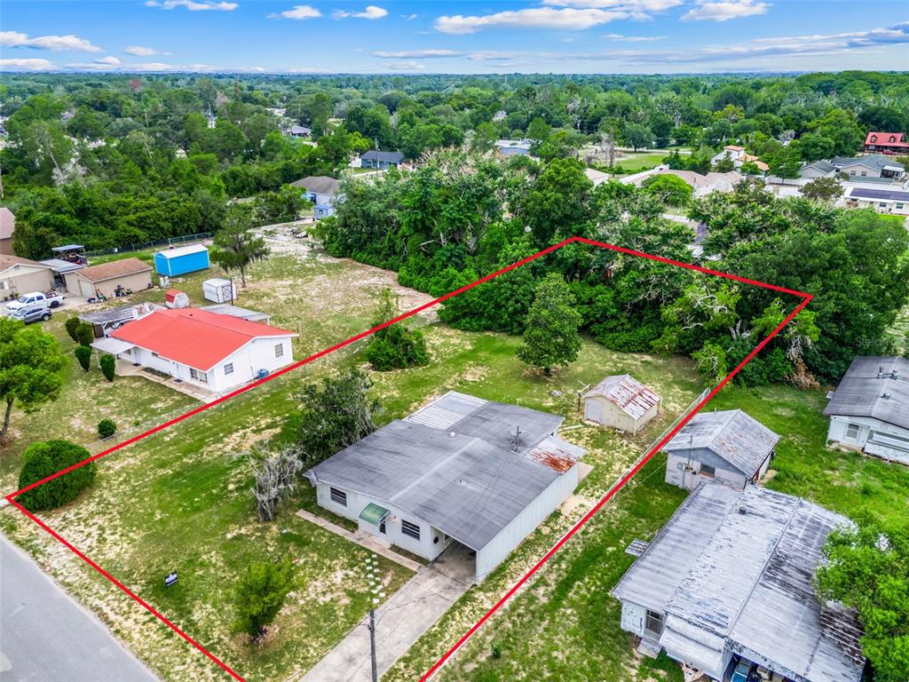 An aerial view shows a single-story house with a carport and a shed on a lot — 11411 HUGGINS ST, LEESBURG, FL