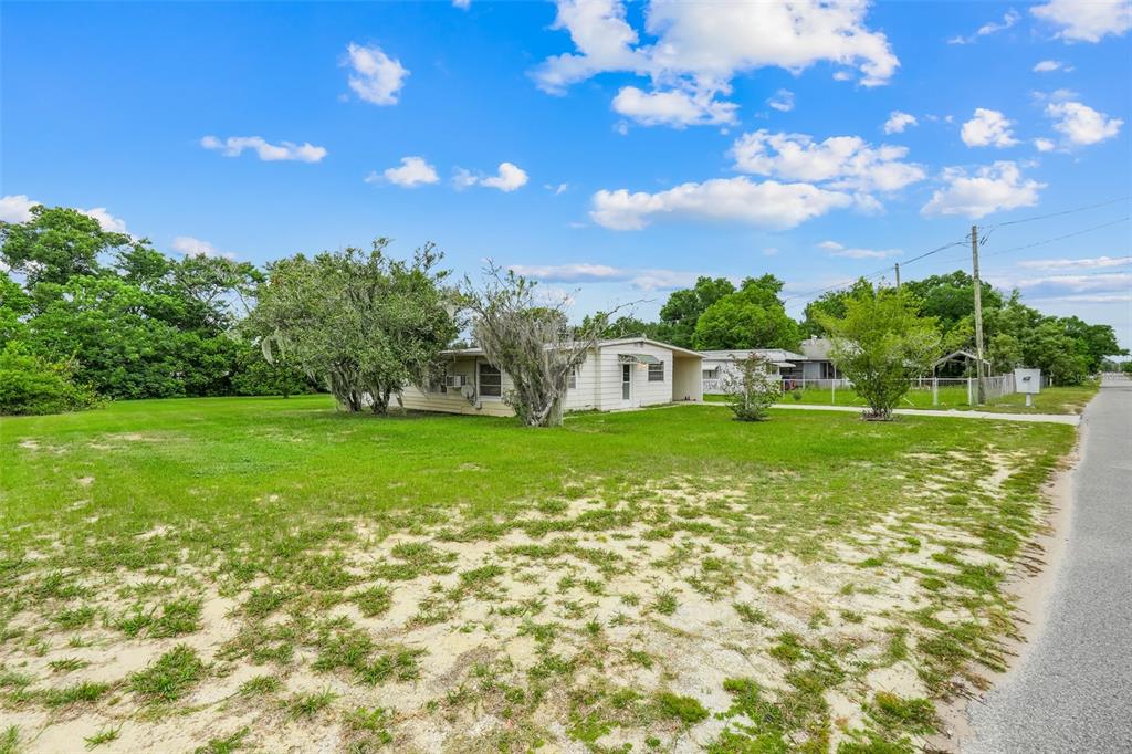 A single-story house with light-colored siding sits on a large, grassy lot near a road — 11411 HUGGINS ST, LEESBURG, FL