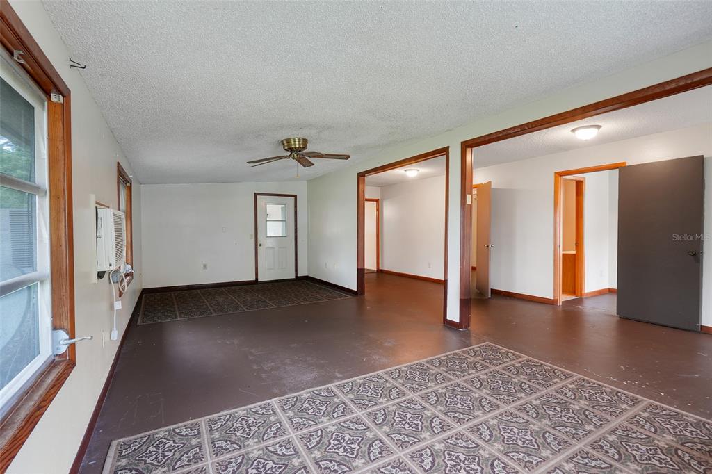 A living room with brown painted floors, patterned area rugs, and a ceiling fan — 11411 HUGGINS ST, LEESBURG, FL