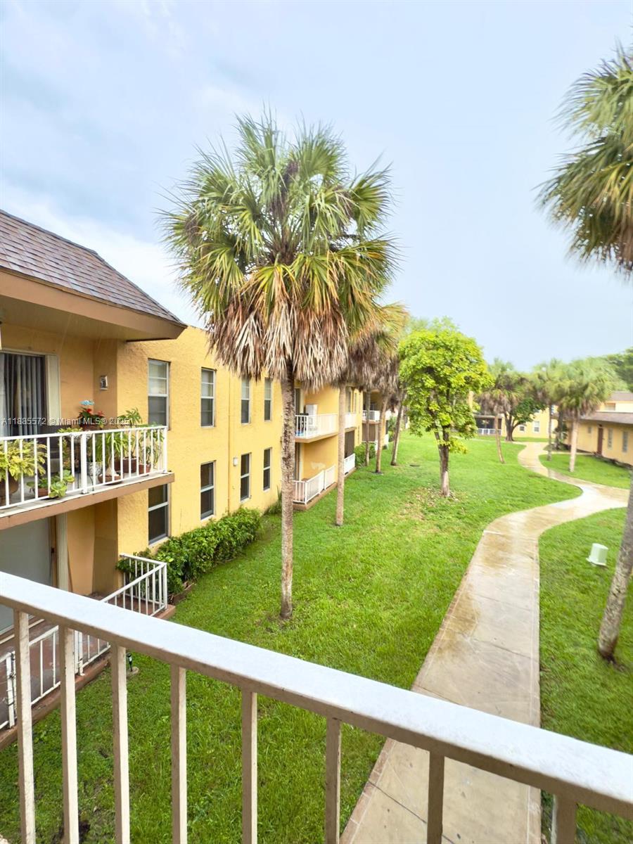 A view from a balcony overlooking a grassy courtyard with palm trees and a walkway — 13700 SW 62nd St # 250, Miami FL 33183, MIAMI, FL