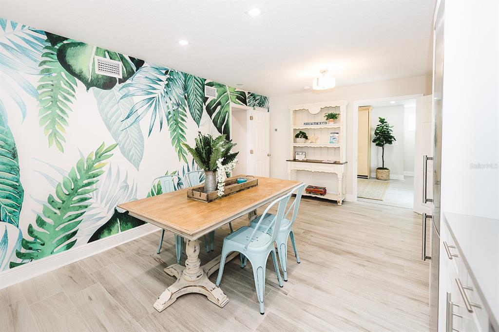 A dining room features a tropical leaf wallpaper accent wall, light wood table, and chairs — 106 E BAY DRIVE, TREASURE ISLAND, FL