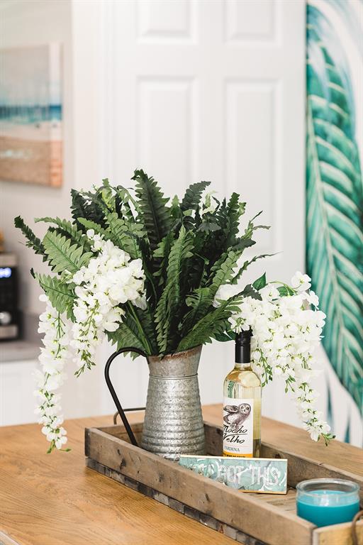 A wooden tray on a table holds a metal pitcher with greenery and a wine bottle — 106 E BAY DRIVE, TREASURE ISLAND, FL