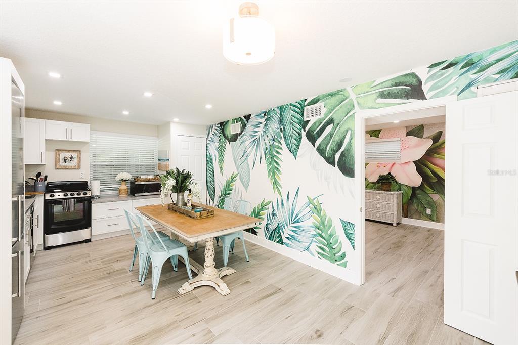 A dining area features a wooden table, light blue chairs, and a tropical leaf mural — 106 E BAY DRIVE, TREASURE ISLAND, FL